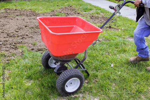 Fototapet An individual sowing lawn grass seeds with drop lawn spreader in residential bac