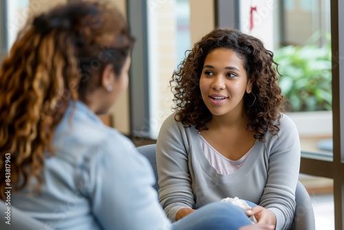 A photo of an African American woman and Hispanic female student sitting in chairs talking to each other during a therapy session at a university center for mental health support.