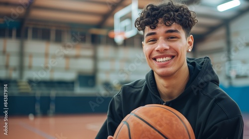 Smiling young man holding a basketball in an indoor court. Sports and youth concept.