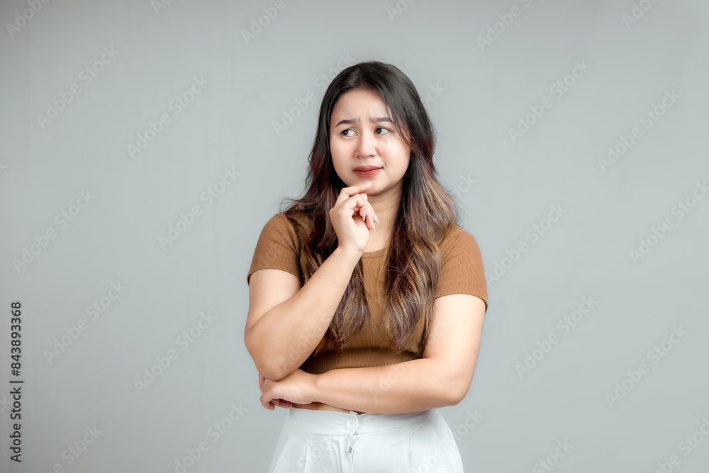 Studio portrait of a beautiful young Asian Indonesian woman thinking about something while standing and holding her chin. Isolated Studio portrait of a beautiful young Asian Indonesian woman thinking about something while standing and holding her chin. Isolated