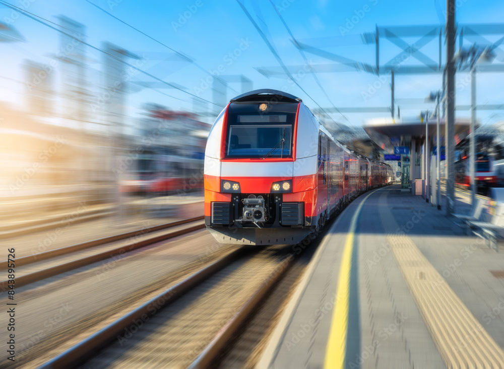 High-speed red passenger train moving at railway station platform under clear blue sky at sunset. Train station. Modern railway transportation concept with blurred motion effect. Railroad. Commercial High-speed red passenger train moving at railway station platform under clear blue sky at sunset. Train station. Modern railway transportation concept with blurred motion effect. Railroad. Commercial