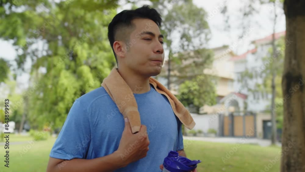 Medium shot of sporty man of Asian ethnicity drinking water after intensive training in local park Medium shot of sporty man of Asian ethnicity drinking water after intensive training in local park