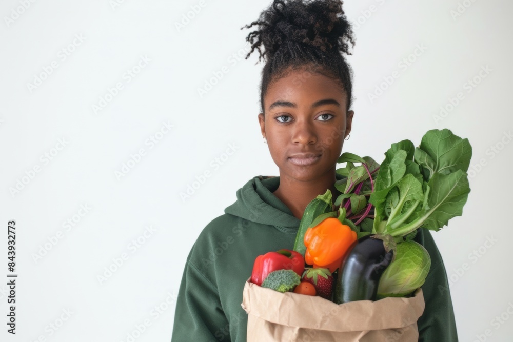 diverse black woman in green hoodies with paper bag full of vegetables isolated on minimal white gray background smiling after grocery shopping at eco market, 0km food concept diverse black woman in green hoodies with paper bag full of vegetables isolated on minimal white gray background smiling after grocery shopping at eco market, 0km food concept