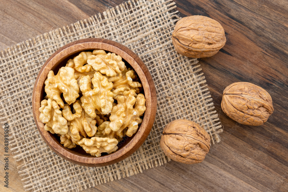 Overhead view of a bowl full of walnut kernels on a wooden surface. A piece of burlap and a few shelled walnut lying around Overhead view of a bowl full of walnut kernels on a wooden surface. A piece of burlap and a few shelled walnut lying around