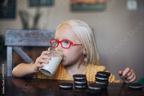 Little blond girl with red glasses with a glass of molk and oreo cookies photo