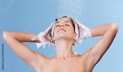 Shower, water and woman washing hair for shampoo, cosmetics and wellness cleaning or conditioner. Female person, soap foam and rinsing scalp in studio blue background for haircare or morning routine