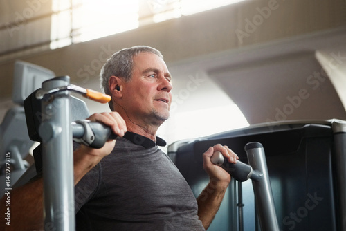 Mature man, chest press and workout with machine for fitness, training or indoor exercise at gym. Active male person with earphones on equipment for strength, muscle gain or wellness at health club