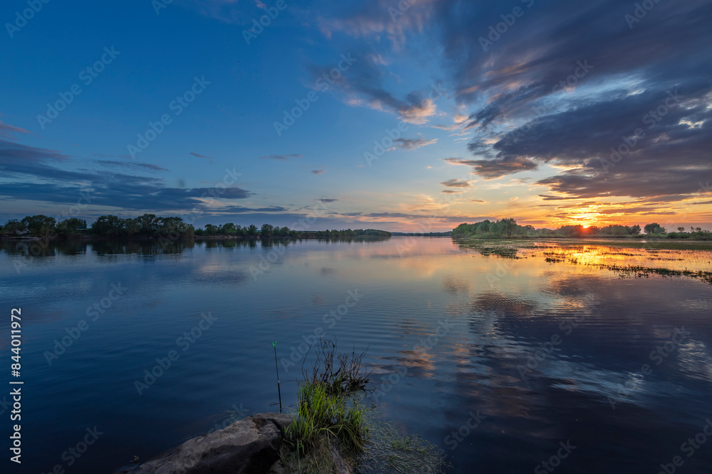 Fototapeta premium A scenic view of a river at sunset, with a peaceful and calming atmosphere. The water reflects the golden hues of the sky, creating a beautiful and serene image.