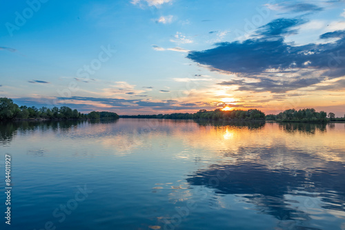 The sun is casting a warm golden glow as it sets over the calm waters of a lake, creating a serene and magical atmosphere.