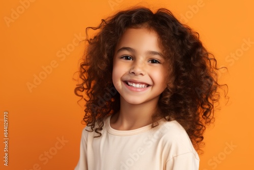 Portrait of a cheerful little girl with curly hair over orange background