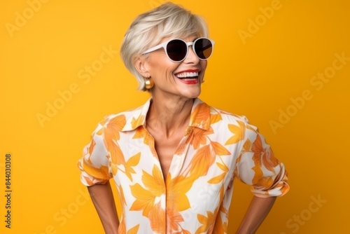 Portrait of a happy senior woman in sunglasses over yellow background.