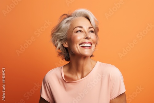 Portrait of a happy senior woman laughing and looking up on orange background
