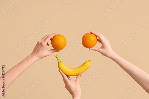 Hands making happy face with fresh oranges and banana on beige background
