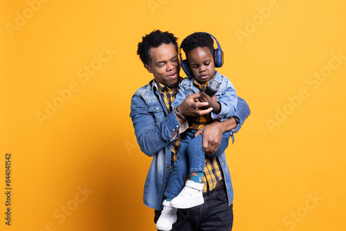 Canvas Print African american father and son playing with a flashlight in studio, cute toddler wearing headphones while his dad is carrying him around
