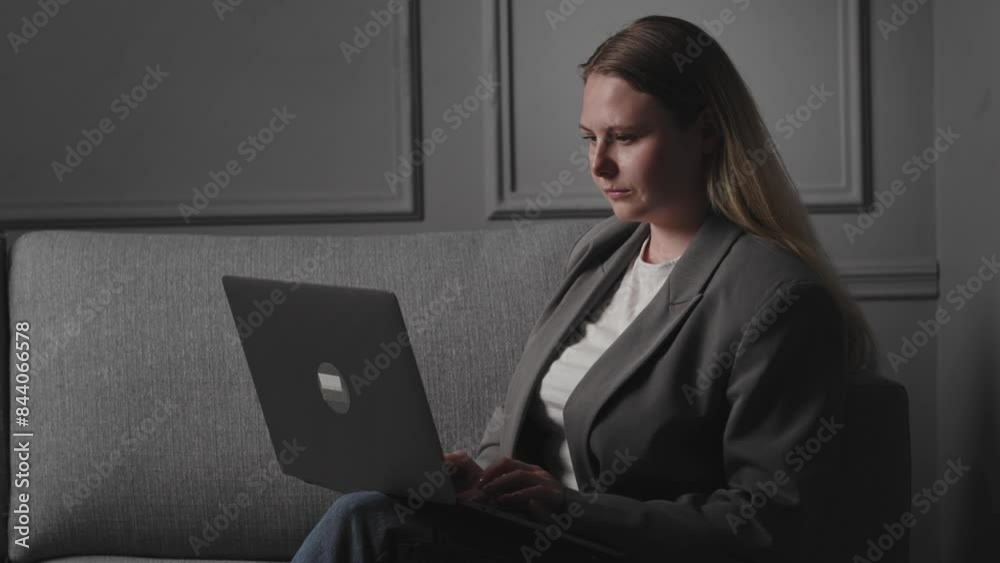 A young serious and concentrated blonde girl blogger, student or entrepreneur sits sideways on the sofa at home in the apartment, uses a laptop for remote work or study, types, maintains business A young serious and concentrated blonde girl blogger, student or entrepreneur sits sideways on the sofa at home in the apartment, uses a laptop for remote work or study, types, maintains business