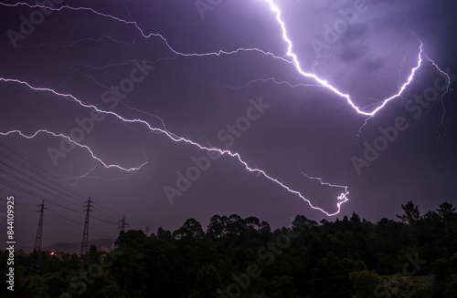 Thunderstorm night with several rays in the sky over the tree line on the horizon.