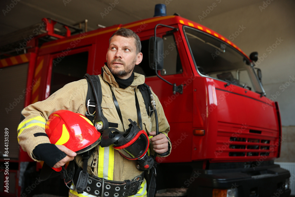 Firefighter in uniform with helmet and mask near red fire truck at station Firefighter in uniform with helmet and mask near red fire truck at station