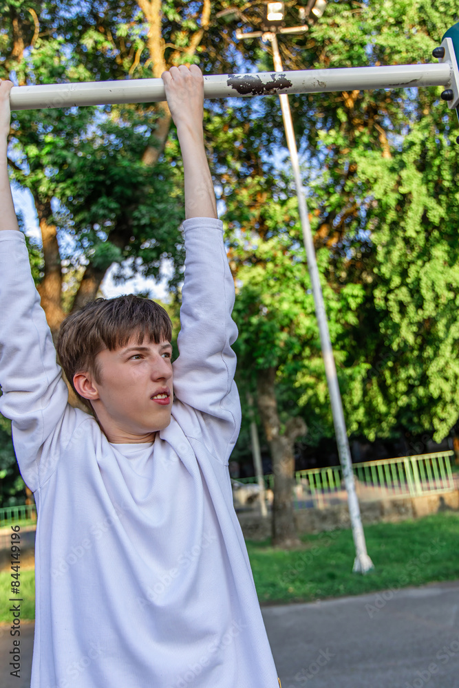 Young Boy Exercising on a Pull Up Bar in a Park on a Sunny Day Young Boy Exercising on a Pull Up Bar in a Park on a Sunny Day