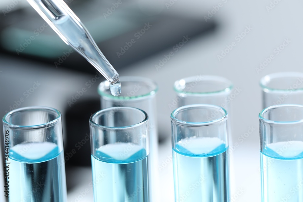 Dripping liquid from pipette into test tube on blurred background, closeup Dripping liquid from pipette into test tube on blurred background, closeup
