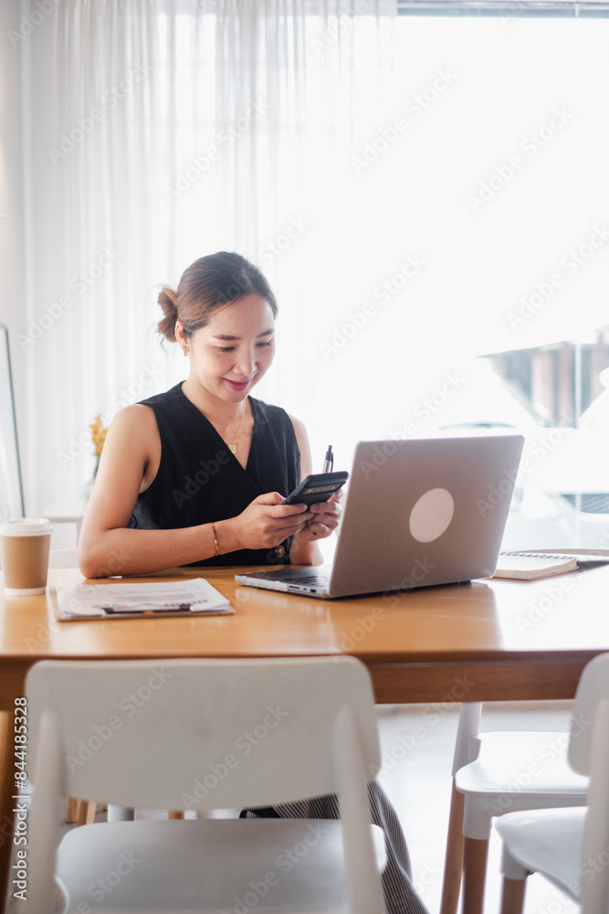 Young woman multitasking with laptop and smartphone at a home office desk, surrounded by coffee and documents. Young woman multitasking with laptop and smartphone at a home office desk, surrounded by coffee and documents.