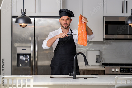 A chef is holding a piece of salmon in his hand and wearing a black hat. High quality photoA chef is holding a piece of salmon in his hand and wearing a black hat. Concept expertise in the kitchen photo