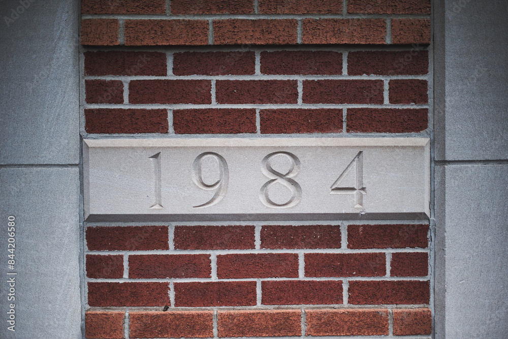 Fototapeta premium Stone plaque with 1984 engraving in brick wall