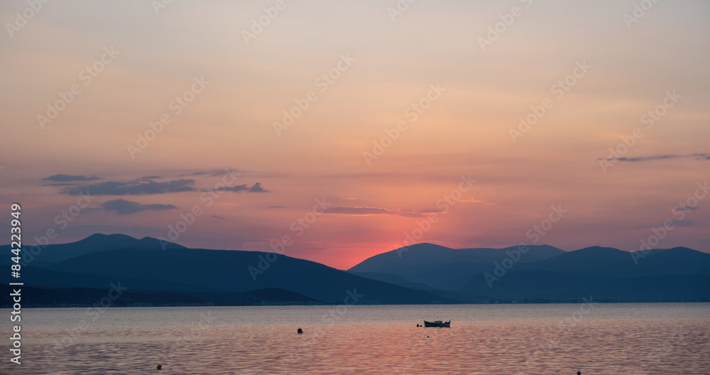 Fototapeta premium Colorful sky pink purple color over sea water. Mountain silhouette, moored boat in open Greek sea.