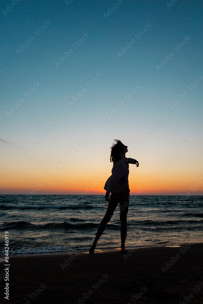 Fototapeta premium girl enjoying a walk on the beach at sunset. Silhouette of a woman looking at the sunset. Summer mood.