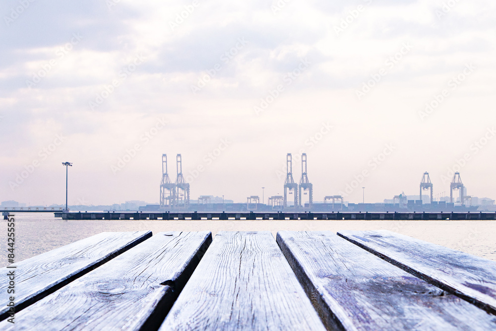 Naklejka premium Empty wooden planks or brown table floor. With port, cranes lift containers and fog covers orange sky and white clouds in morning. Abstract texture background. For place food, drink.