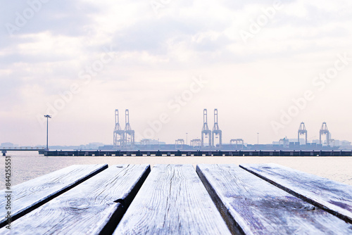 Empty wooden planks or brown table floor. With port, cranes lift containers and fog covers orange sky and white clouds in morning. Abstract texture background. For place food, drink.