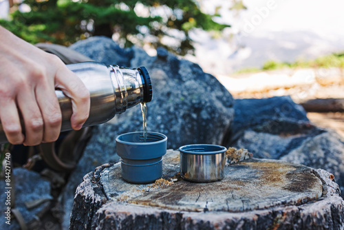 Close-up of male hand pouring hot tea from thermo flask outdoors photo