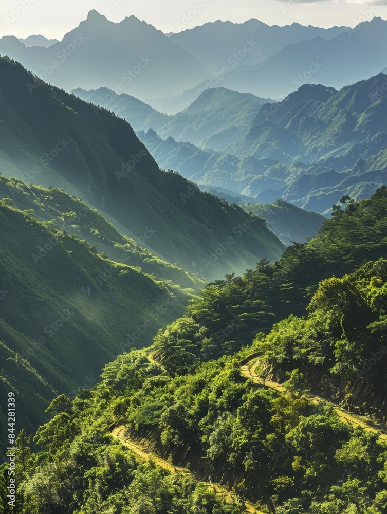 Obraz premium Scenic mountain valley with lush green hills and layered mountain ranges in the background. The picturesque landscape features misty ridges and a serene atmosphere.