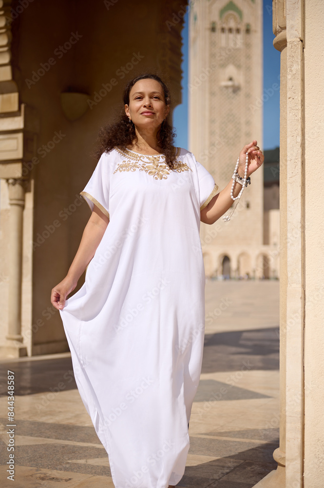 Woman in traditional white dress standing by mosque in bright daylight