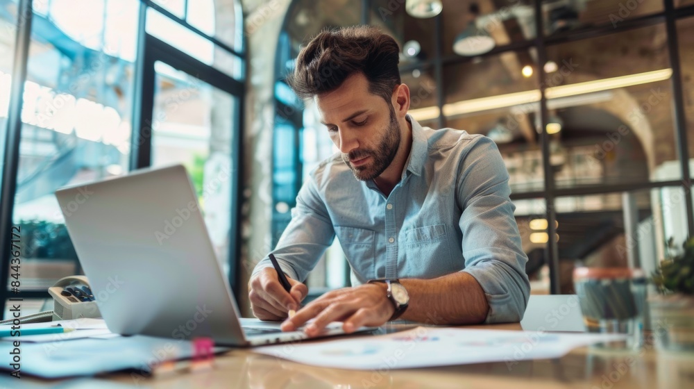Photo of a businessman multitasking in the office He uses the touchpad while reading emails on his laptop and taking notes on paper. Photo of a businessman multitasking in the office He uses the touchpad while reading emails on his laptop and taking notes on paper.