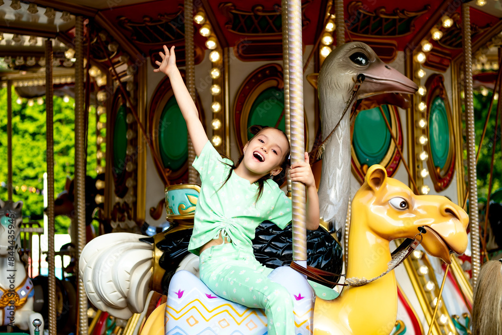 Fototapeta premium a child in an amusement park rides a carousel and enjoys the International Children's Day in summer, happy childhood and holidays