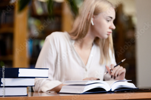 a young woman with blond hair who sits at a table in a library or study hall. concept of learning and self-development. The woman is immersed in the process of reading and analyzing information, which