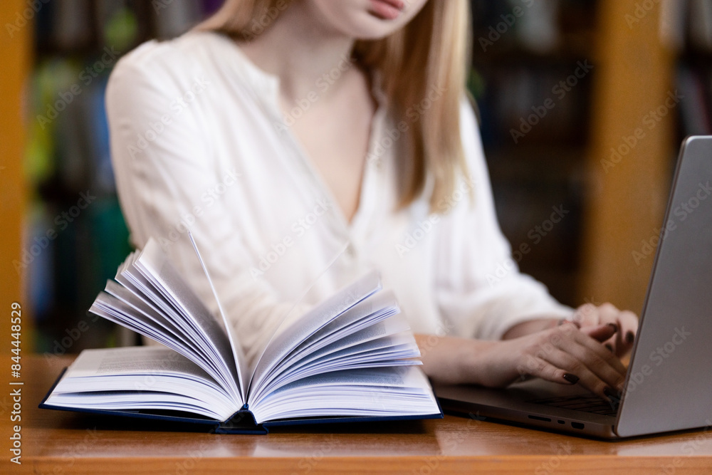 A teenage girl in the library writes an essay or a note, takes notes, prepares for an exam. Study and education concept. A teenage girl in the library writes an essay or a note, takes notes, prepares for an exam. Study and education concept.