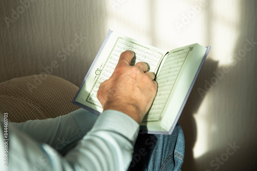 Hands of senior man holding Quran at home. Natural aesthetic light. photo