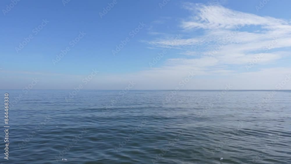 A stretch of calm blue sea under a blue and slightly cloudy sky A stretch of calm blue sea under a blue and slightly cloudy sky