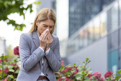 Картината върху платно Businesswoman sneezing outdoors surrounded by plants, possibly due to allergies or cold symptoms