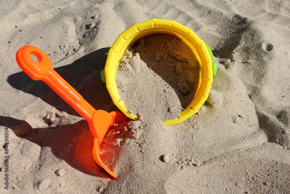 closeup of a small orange plastic shovel stuck in the sand next to a yellow plastic bucket filled with sand in the sandpit closeup of a small orange plastic shovel stuck in the sand next to a yellow plastic bucket filled with sand in the sandpit