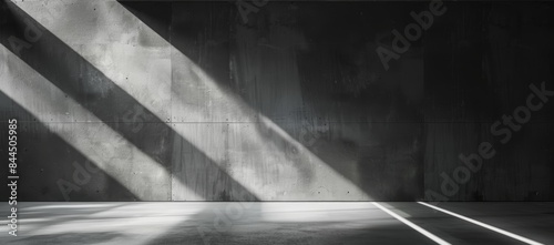 A wide shot of an empty room with a concrete floor and wall. The sun is shining through a window, casting long diagonal shadows across the room