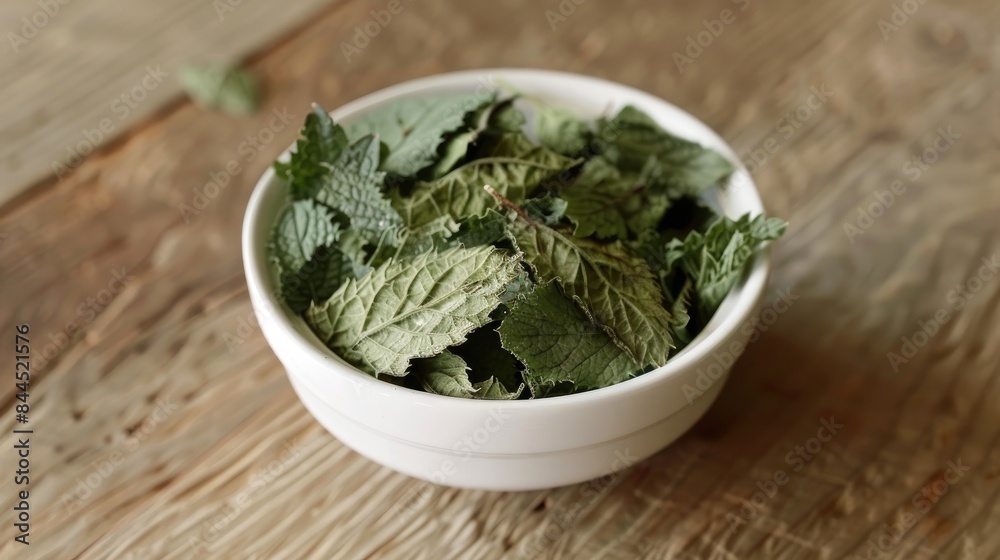 Lemon balm leaves that have been dried are placed in a white bowl on a wooden surface Lemon balm leaves that have been dried are placed in a white bowl on a wooden surface