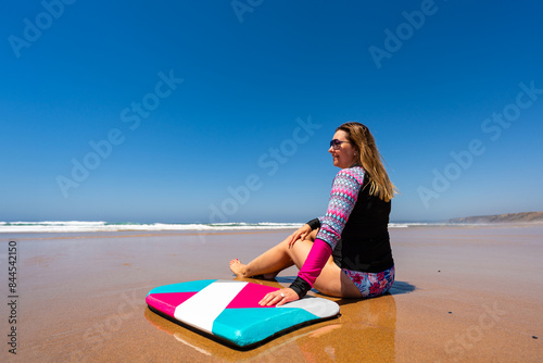 Beautiful woman holding bodyboard  sitting on sunny beach Bordeira praia, Algarve , Portugal