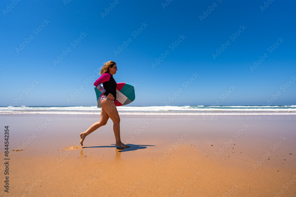 Beautiful woman holding bodyboard running on sunny beach Bordeira praia, Algarve , Portugal Beautiful woman holding bodyboard running on sunny beach Bordeira praia, Algarve , Portugal