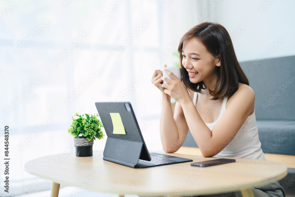 Young Woman Enjoying Coffee While Working on Laptop at Home, Smiling and Relaxed, Modern Home Office Setup with Green Plant on Wooden Table, Casual and Comfortable Lifestyle Young Woman Enjoying Coffee While Working on Laptop at Home, Smiling and Relaxed, Modern Home Office Setup with Green Plant on Wooden Table, Casual and Comfortable Lifestyle