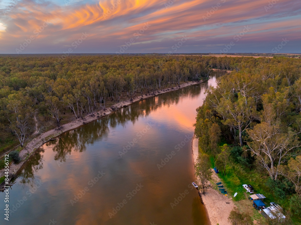 Aerial view of a river lined with trees and a colourful sunset sky overhead