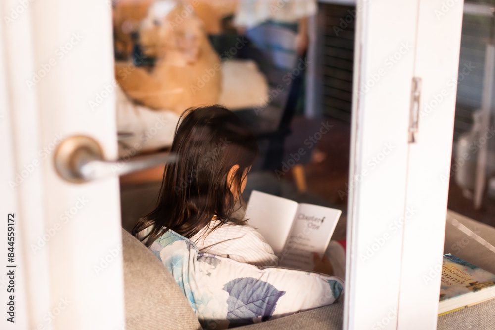 a young little girl reading a book on the couch a young little girl reading a book on the couch