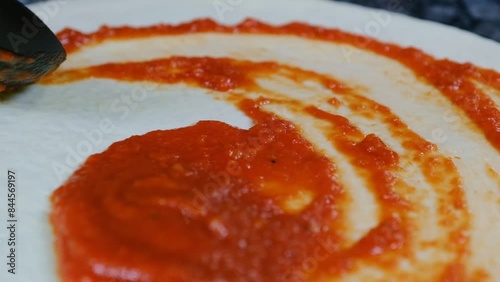 Chef in black gloves spreads red sauce with a spoon over pizza dough slow motion close-up