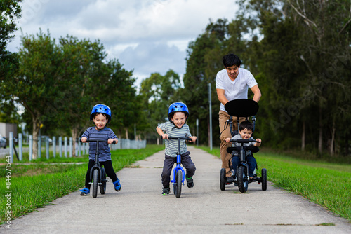 Chinese Australian dad on walk with his sons riding balance bikes on footpath